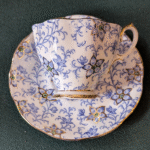 This vintage china cup and saucer set is a stunning example of delicate craftsmanship and timeless beauty. Featuring a graceful scalloped edge, the set is adorned with a detailed blue floral pattern highlighted with touches of green and finished with gleaming gold trim. Both the cup and saucer carry a refined charm that makes them perfect for collectors or for serving tea with elegance. Beautiful Design: Intricate blue floral detailing with subtle green highlights. Gold Accents: Polished gold trim on the cup, saucer, and handle for a refined finish. Vintage Appeal: A true collectible, ideal for adding charm to any china collection. Versatile Use: Perfect for display in a cabinet, a vintage-inspired tea party, or as a thoughtful gift. With its unique pattern and fine detailing, this china set is more than tableware—it’s a statement of elegance and heritage.